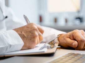 Close-up of hands writing on a clipboard with a pen, indicating professional documentation in a healthcare setting.