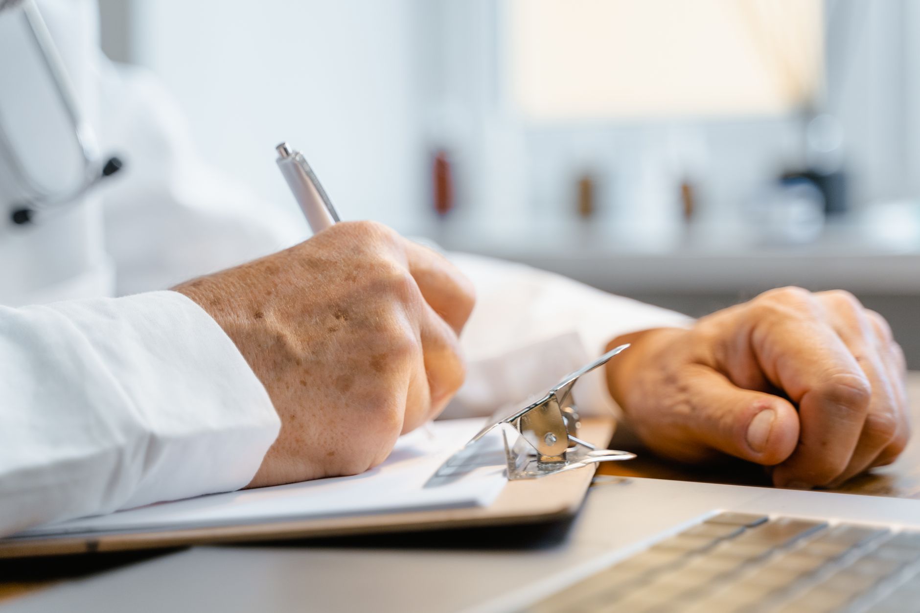 Close-up of hands writing on a clipboard with a pen, indicating professional documentation in a healthcare setting.